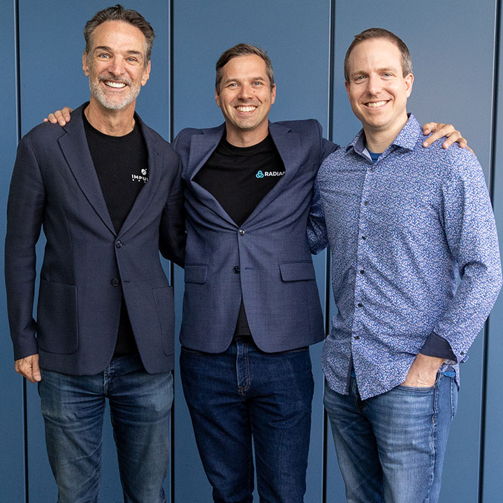 Three men standing in front of a blue wall, smiling at camera